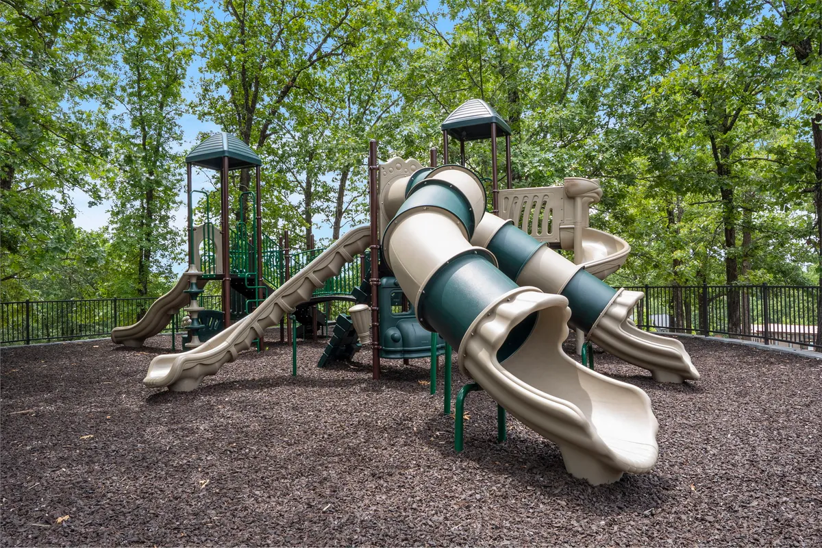 A colorful playground with slides and a climbing structure stands under tall trees, with children playing, parents watching, and families gathering for a picnic. The scene radiates joy and energy, emphasizing the resort's family-friendly atmosphere.