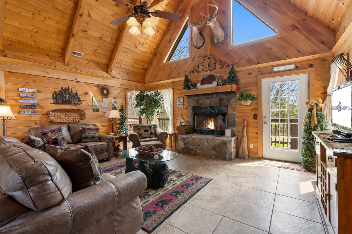 The image showcases the inviting interior of a real log cabin, with a cozy fireplace as the focal point, surrounded by plush leather sofas and rustic wooden ceilings. Warm lighting and tasteful wall art create a welcoming atmosphere perfect for relaxing, socializing, and enjoying quiet moments together.