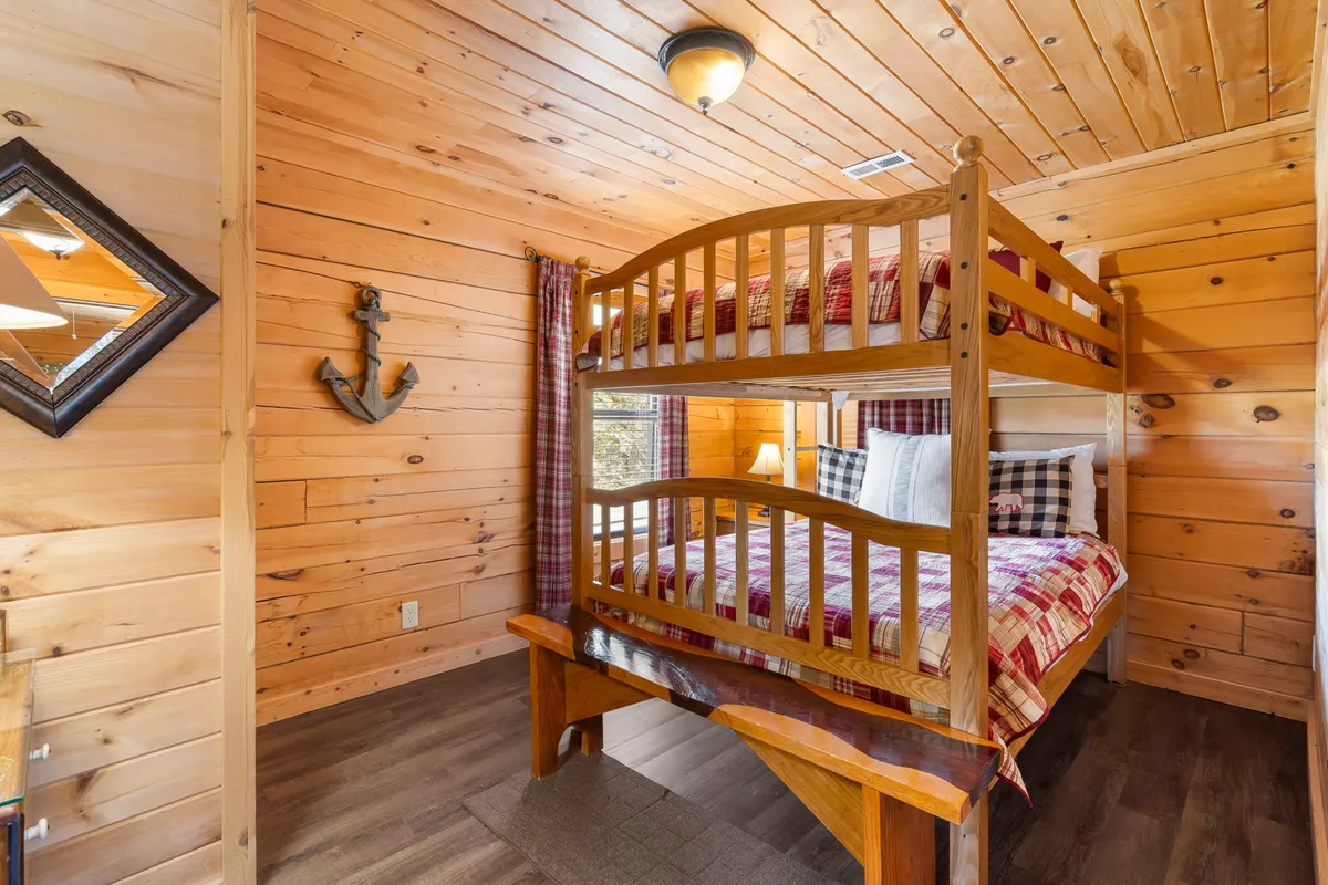 A family-friendly bedroom featuring full-over-full bunk beds, anchor wall decor, plaid bedding, and wooden interiors. The space is bright and welcoming, ideal for kids or groups sharing a room.