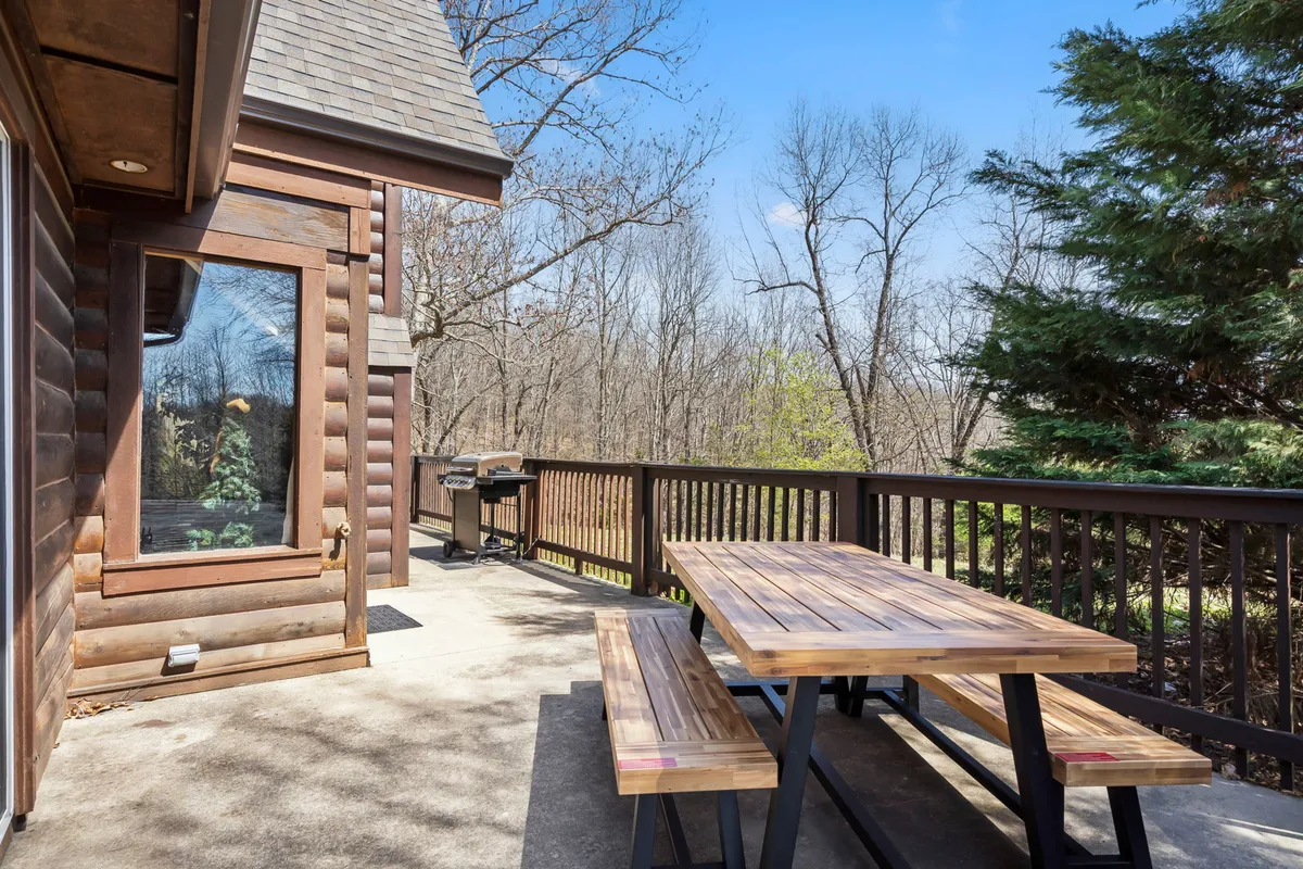 A cozy outdoor dining area featuring a wooden picnic table and grill, set amidst tall trees. The space is inviting, perfect for barbecues, outdoor meals, and relaxed conversations in nature.