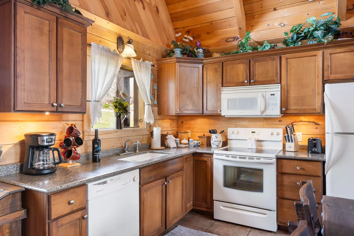 A kitchen scene with wooden cabinets, granite countertops, modern appliances, and a window bringing in natural light. Decorative plants add a touch of homeliness, while the setup invites both morning coffees and festive cooking sessions.