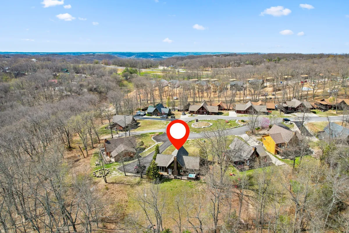 A central building is surrounded by cabins and greenery, with a circular driveway and distant hills creating a communal, nature-focused setting. The scene suggests walkable, open spaces ideal for dog walking, running, and outdoor play.